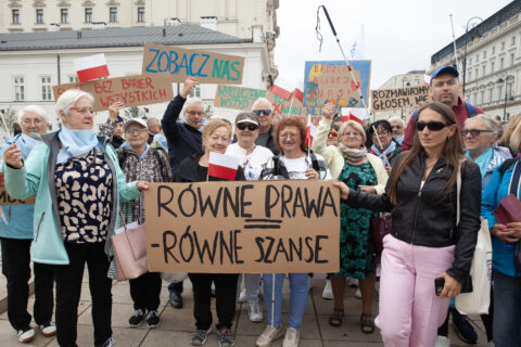 Tłum uczestników manifestacji w Warszawie z transparentem „Równe prawa – równe szanse” i tabliczkami „Zobacz nas”.